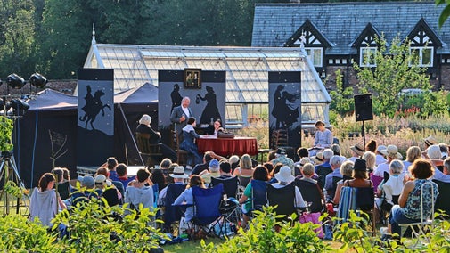 A group of people sat on the grass looking at a stage with actors performing
